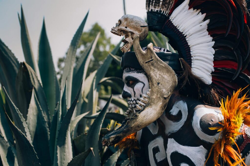 Native Mexican Aztec warrior, with pre-Hispanic makeup simulating a skull and a bone headdress adorned with feathers and cempazuchil flowers